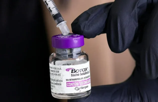Mano con guante negro cargando jeringa en frasco de Botox toxina botulínica Allergan 100 unidades, preparación para tratamiento de rinomodelación en clínica estética Dr. Perdomo