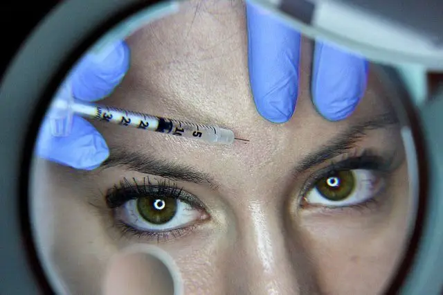 Vista en espejo de aplicación de baby bótox en frente de paciente joven con ojos verdes, técnica preventiva de toxina botulínica en dosis mínimas en clínica estética Dr. Perdomo