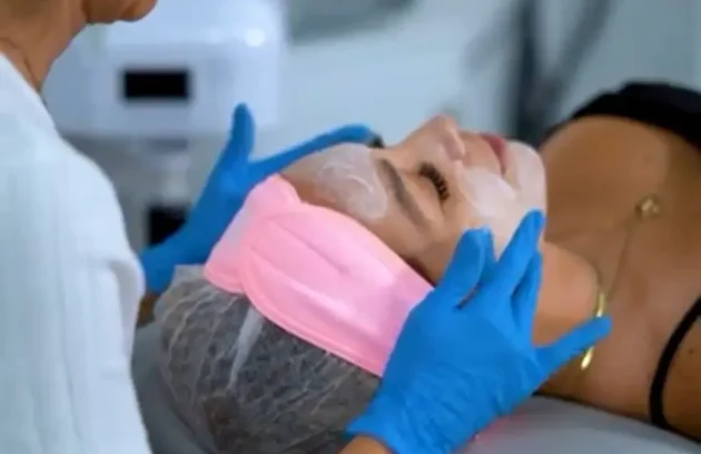 Esteticista aplicando mascarilla facial a paciente recostada en camilla, tratamiento de limpieza y rejuvenecimiento facial previo a eventos especiales en clínica estética Dr. Perdomo