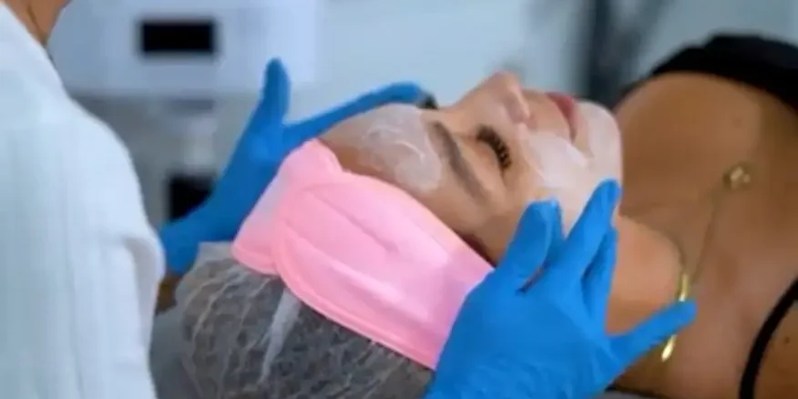 Esteticista aplicando mascarilla facial a paciente recostada en camilla, tratamiento de limpieza y rejuvenecimiento facial previo a eventos especiales en clínica estética Dr. Perdomo