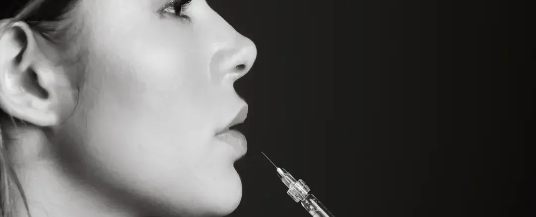 Perfil de mujer con jeringa de relleno dérmico acercándose a labios y mentón, procedimiento estético de Noche Vieja en clínica Dr. Perdomo