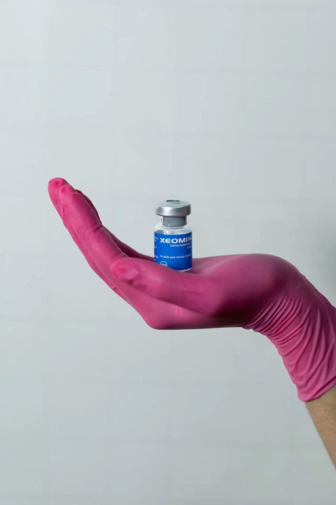 Frasco de Xeomin toxina botulínica sostenido por mano con guante quirúrgico rosa, producto utilizado en tratamientos estéticos faciales en clínica Dr. Perdomo