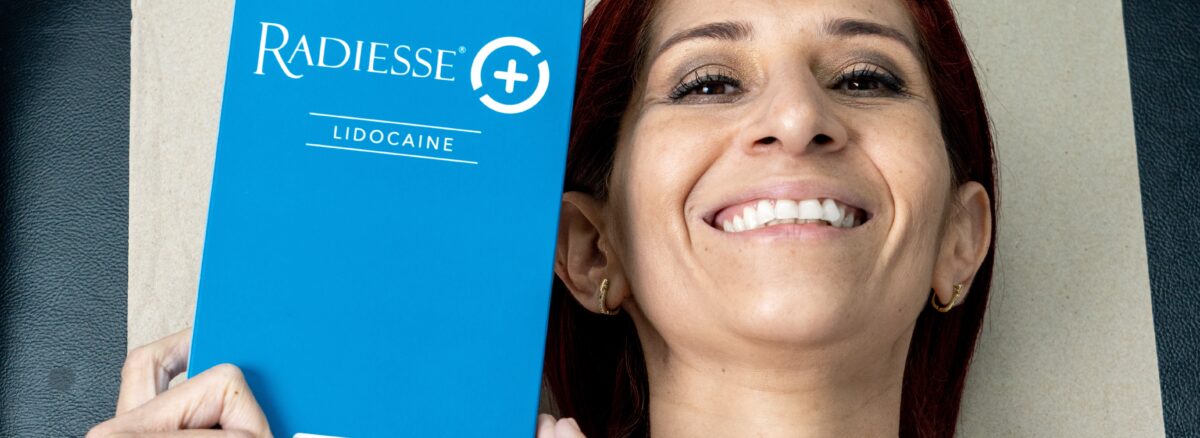 Paciente satisfecha sosteniendo Radiesse antes de su tratamiento de bioestimuladores de colágeno en Clínica Dr. Perdomo